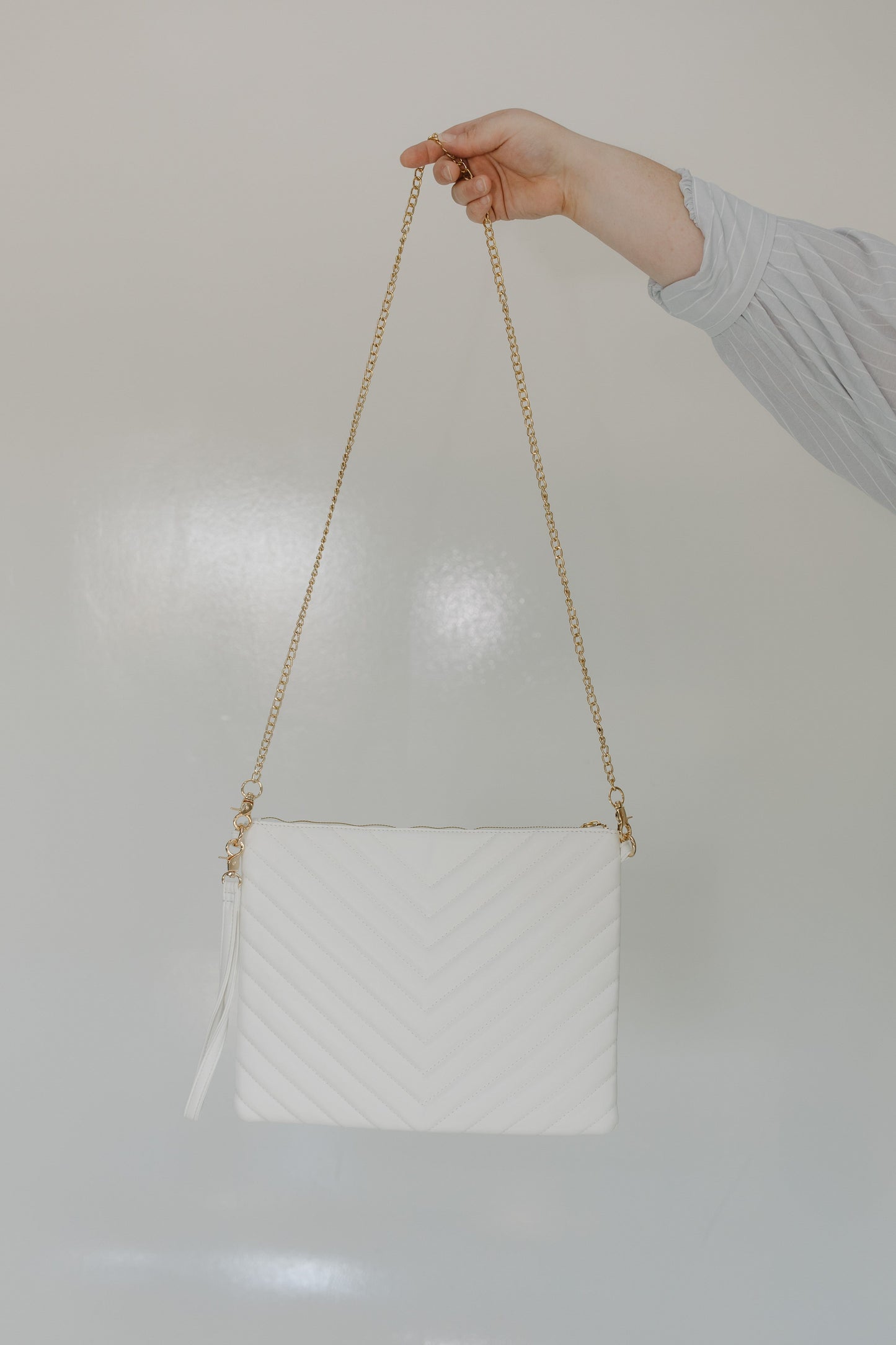 White quilted handbag with a gold chain strap held by a hand against a light background