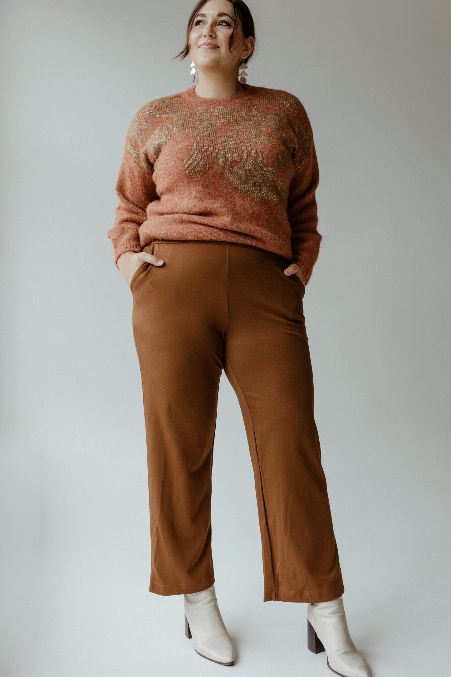 A person stands confidently with hands in pockets, wearing a maroon sweater, Yesta's WIDE LEG TREGGING WITH POCKETS IN TALL featuring a stretchy waistband, and white ankle boots, set against a plain background.