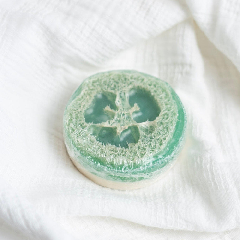 Green loofah sponge soap on a white fabric background