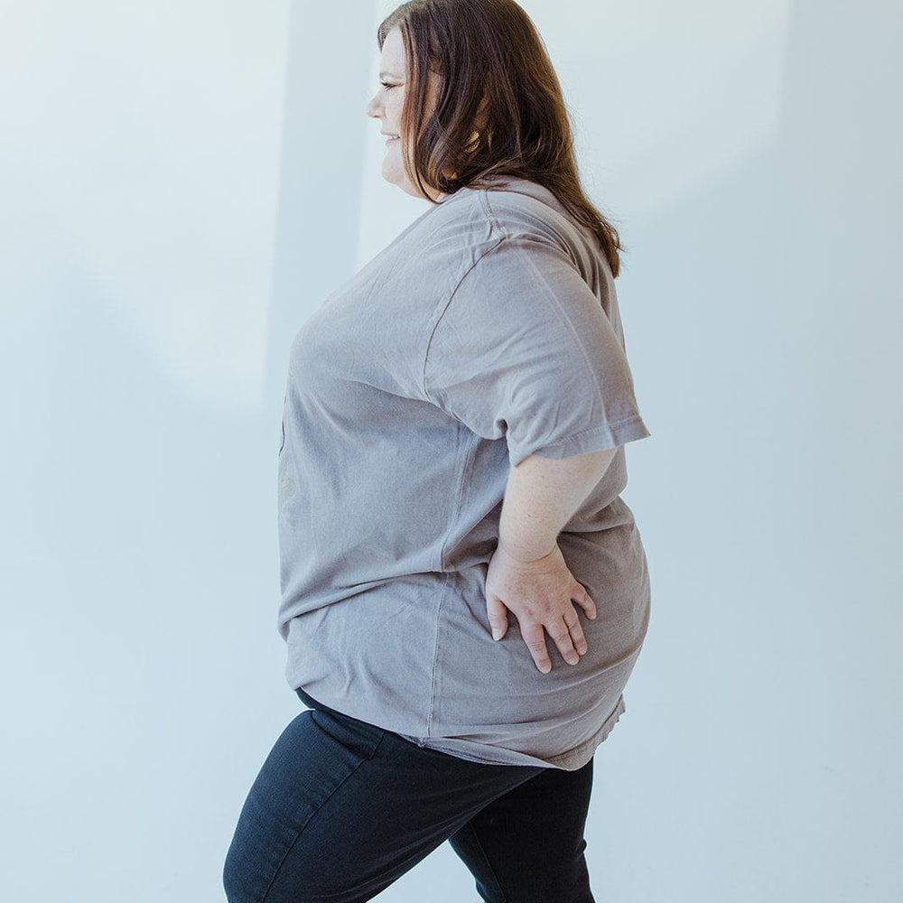 A person wearing the "WORD OF ADVICE DON'T CROSS ME" graphic tee by Love Marlow, paired with black pants, stands sideways in a well-lit room, casually resting a hand on their hip.