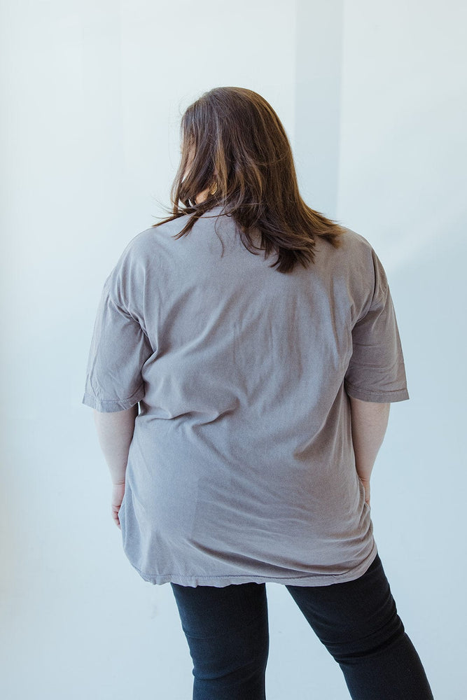 Someone with long hair wearing the "WORD OF ADVICE DON'T CROSS ME" graphic tee by Love Marlow and black pants, displaying a subtle vintage wash as they face away from the camera in a well-lit room.