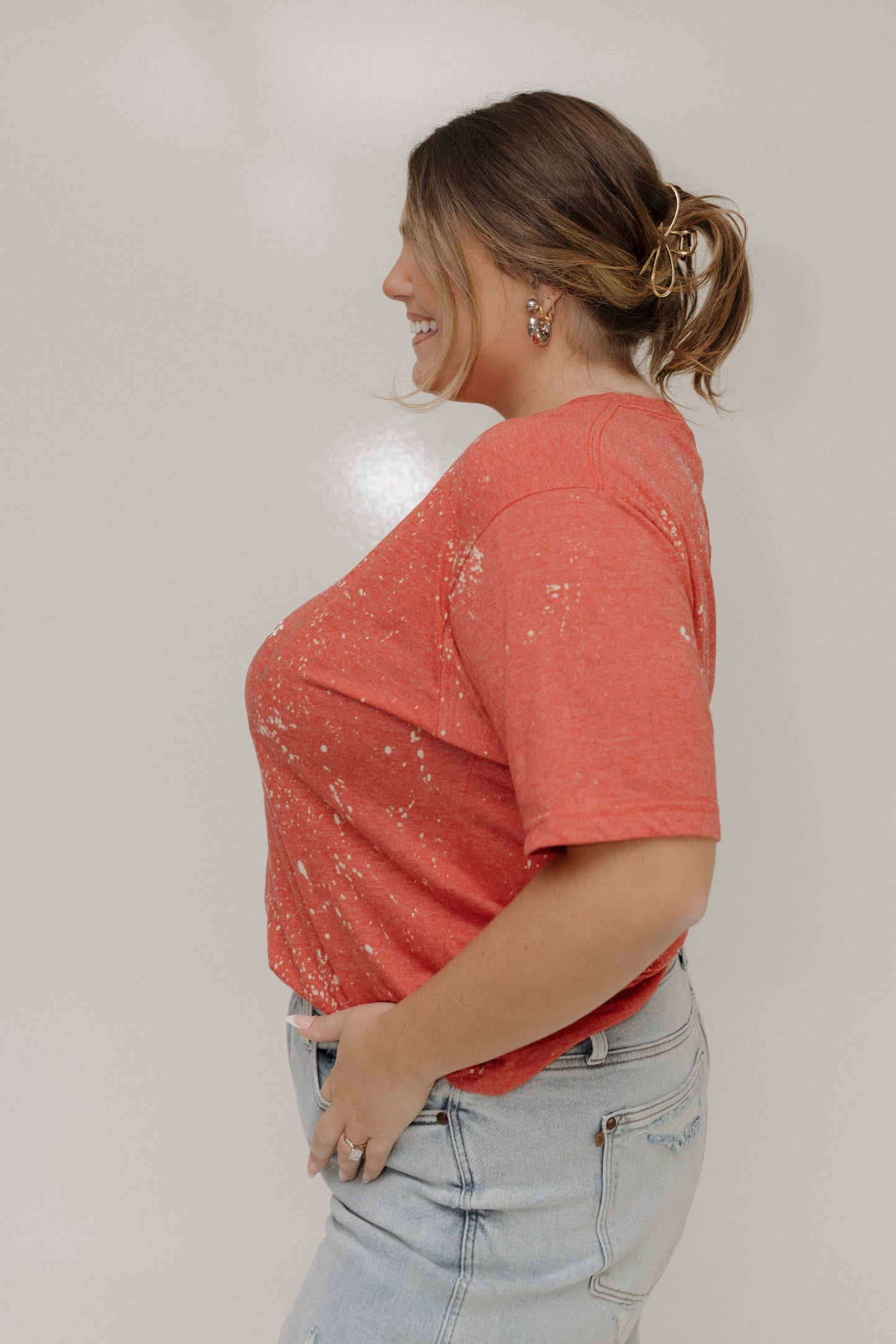 Woman wearing a coral t-shirt with a subtle pattern and light blue jeans against a plain background