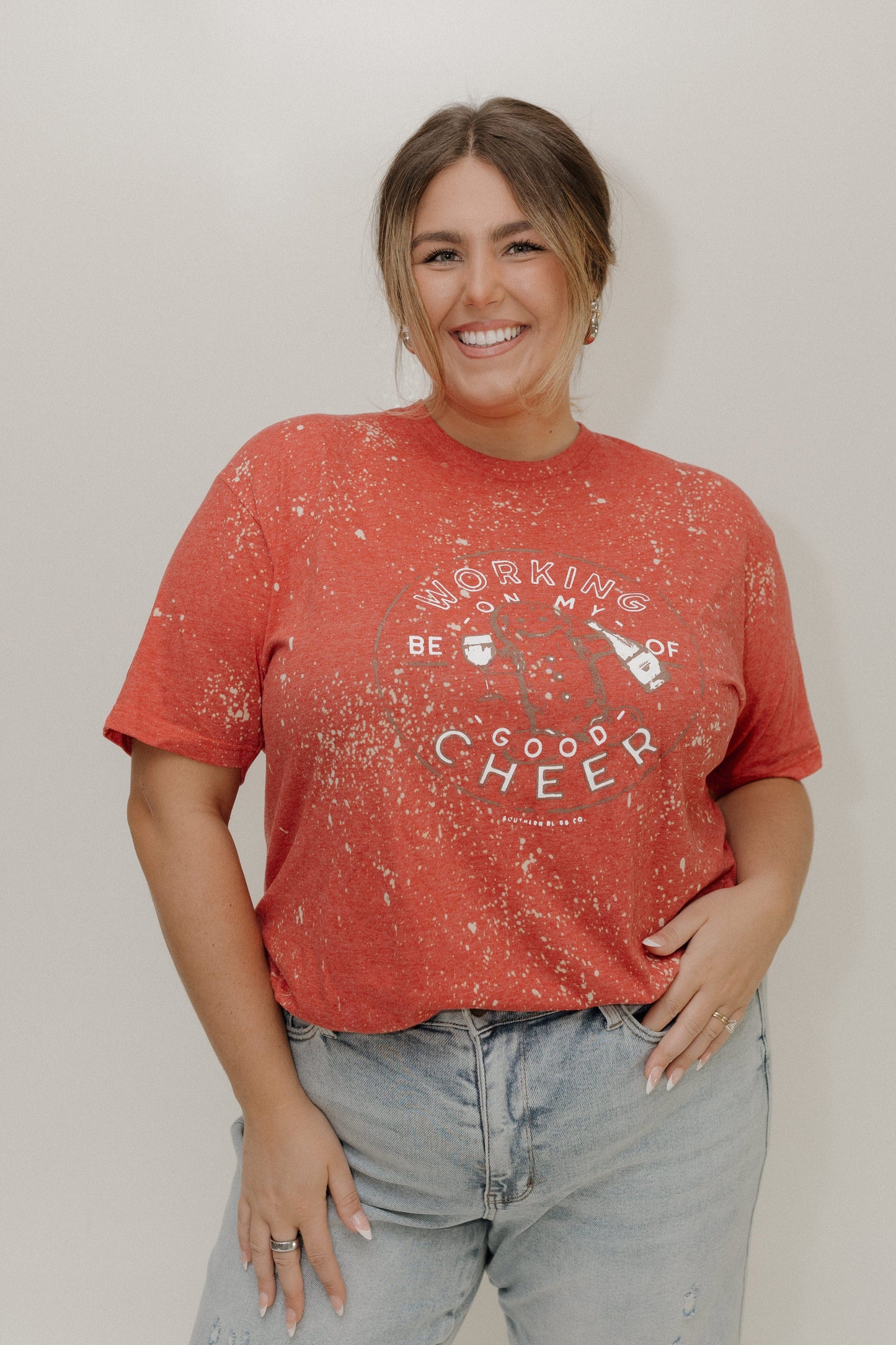 Woman wearing a red t-shirt with text and graphics, standing against a plain background