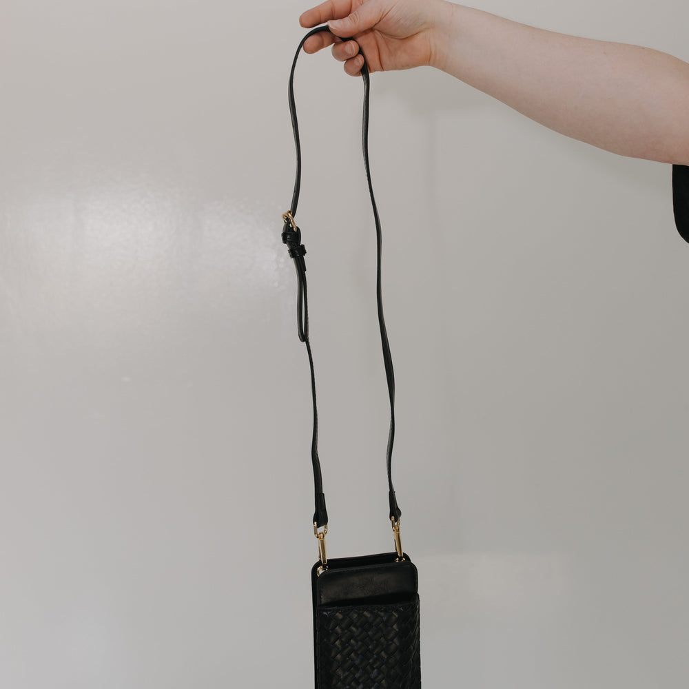 Black handbag with a strap held by a hand against a plain background