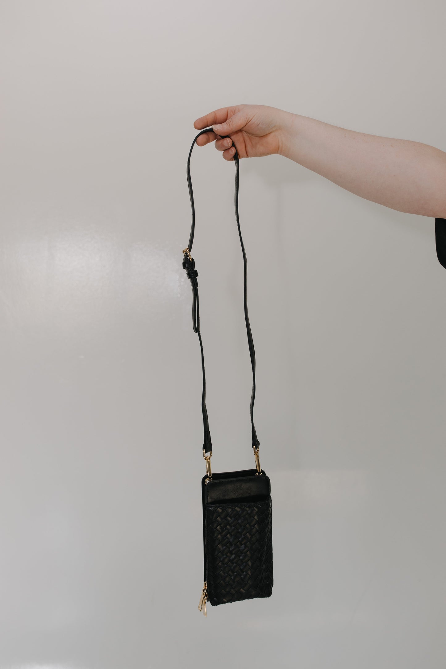 Black handbag with a strap held by a hand against a plain background