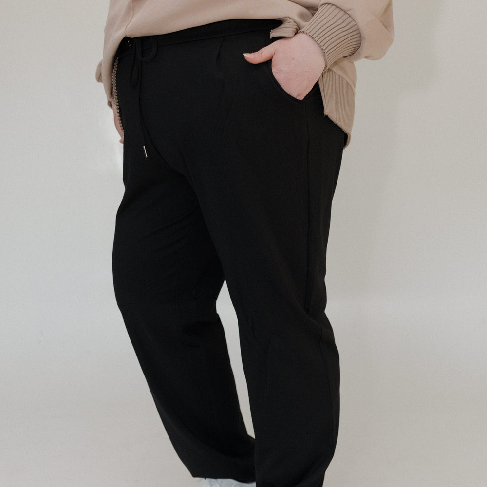 Person wearing a beige sweater and black pants on a plain background