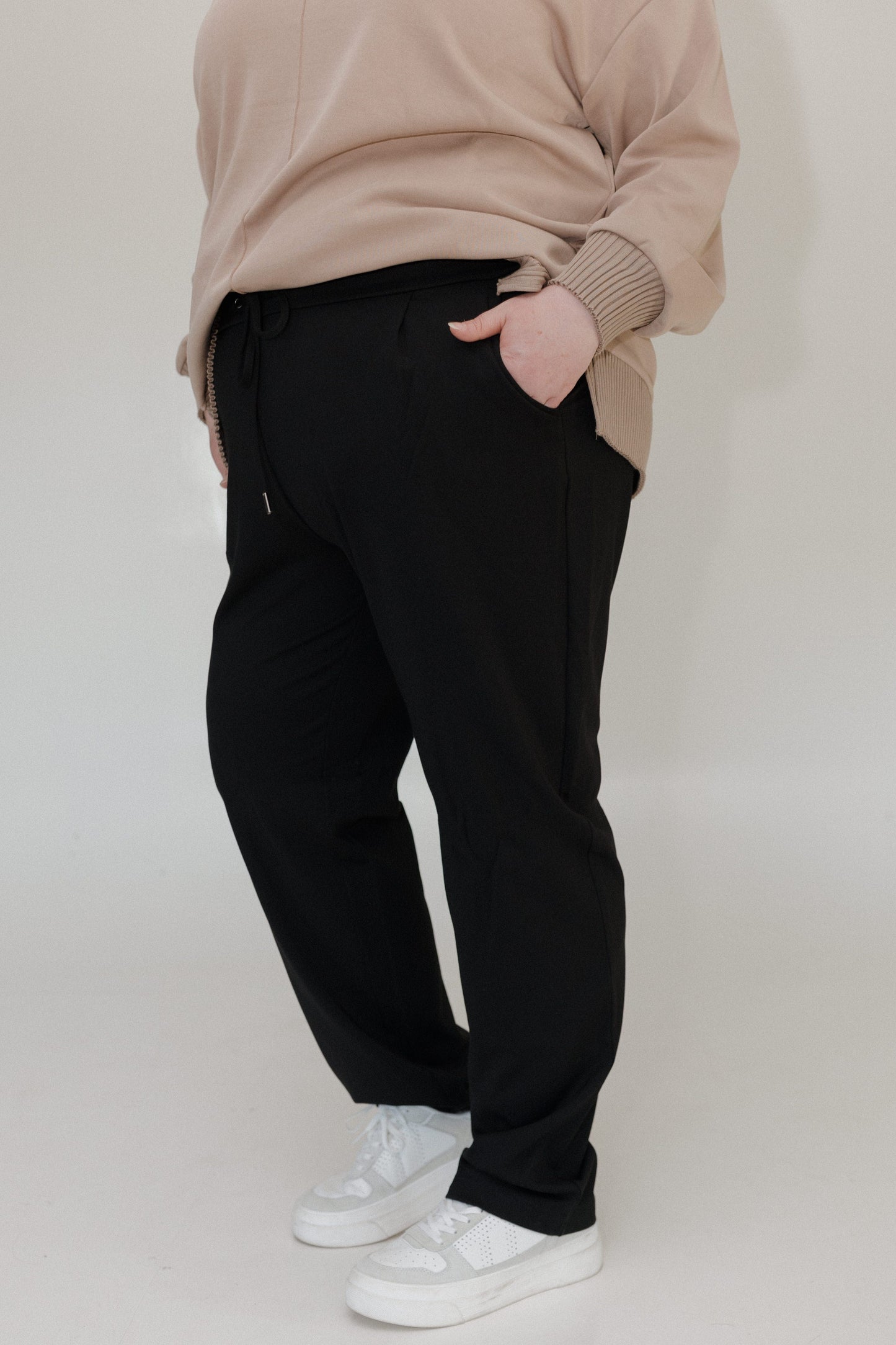 Person wearing a beige sweater and black pants on a plain background
