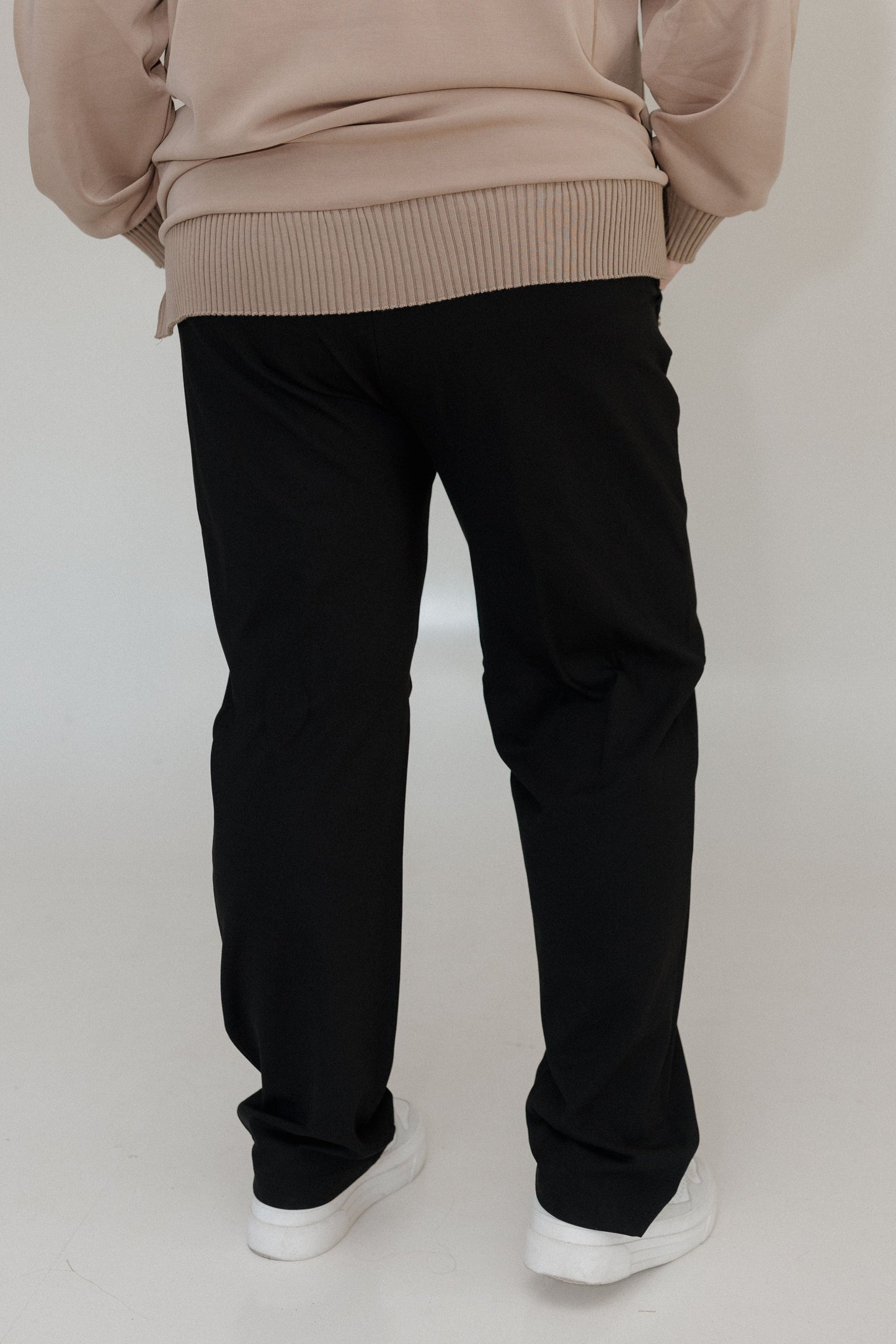Person wearing a beige sweater and black pants on a white background