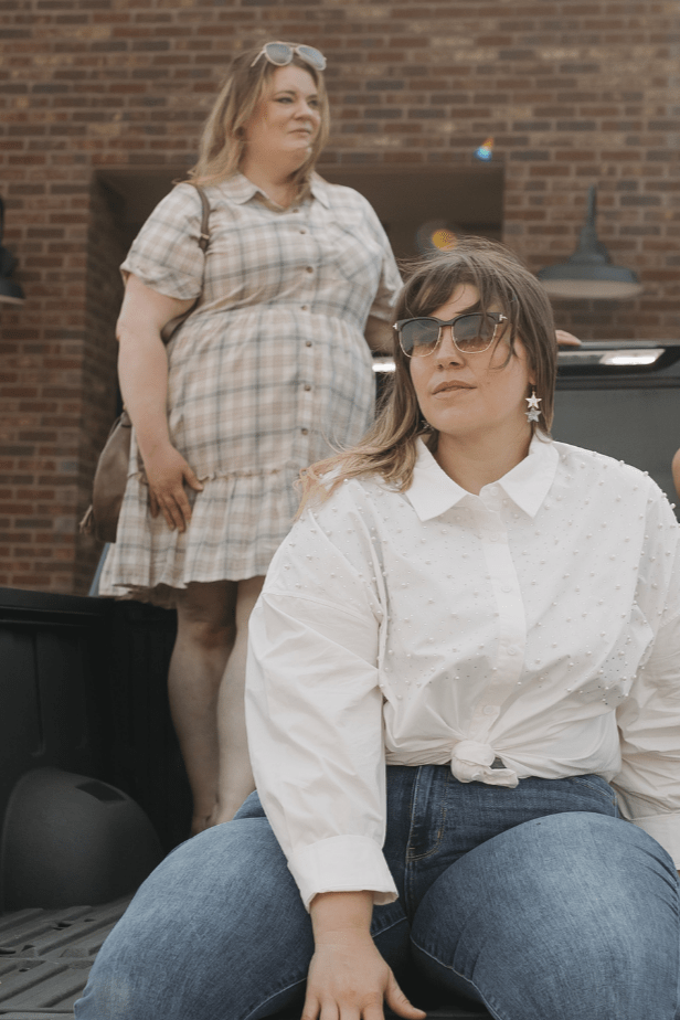Four women standing and sitting on a truck bed in front of a brick building.