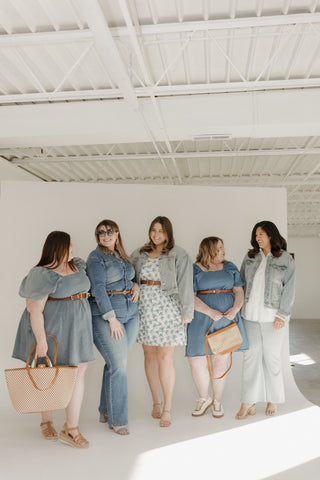 Five women standing in a line wearing denim outfits in a bright room.