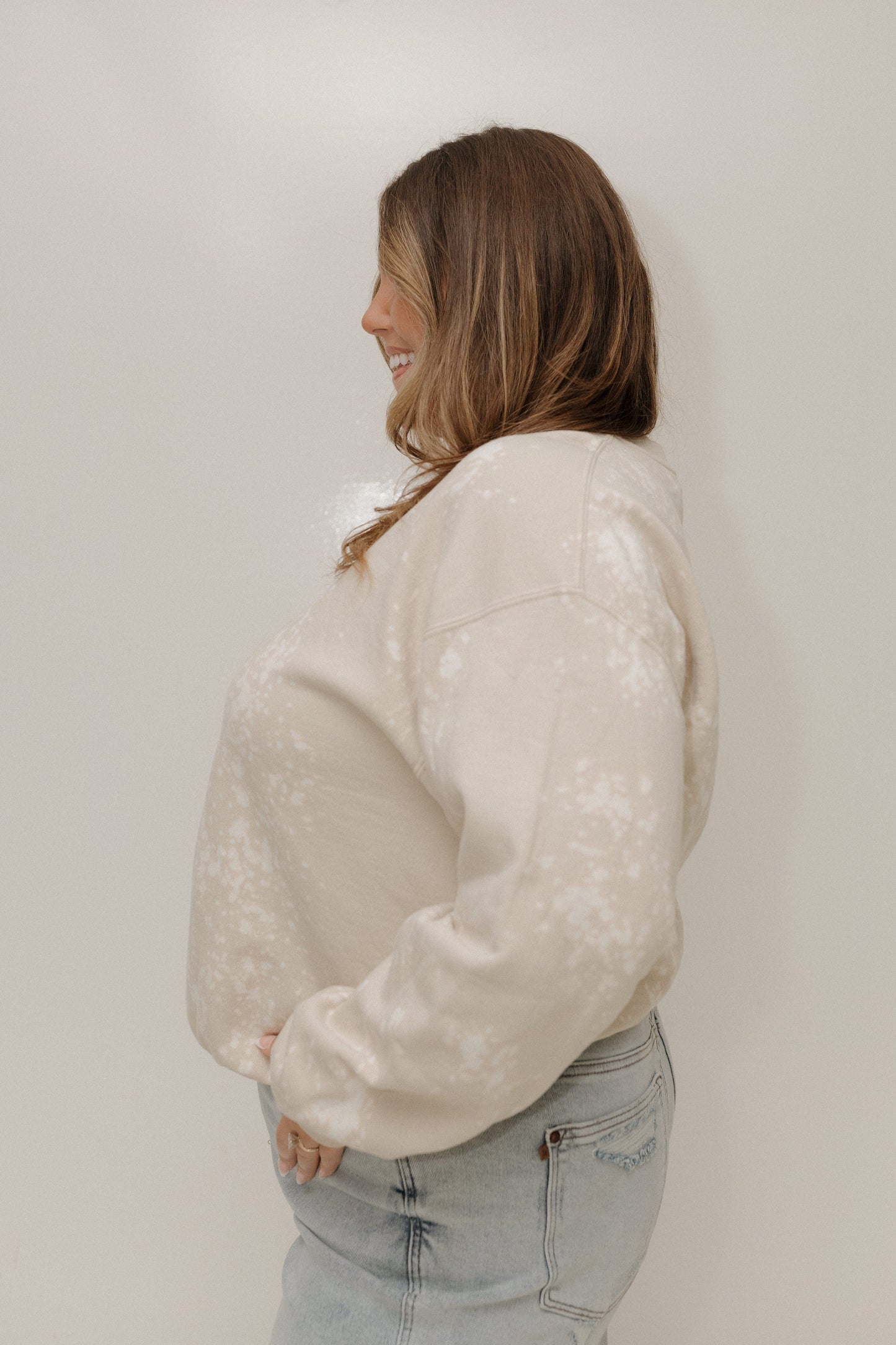 Woman wearing a cream sweater and light blue jeans against a plain background