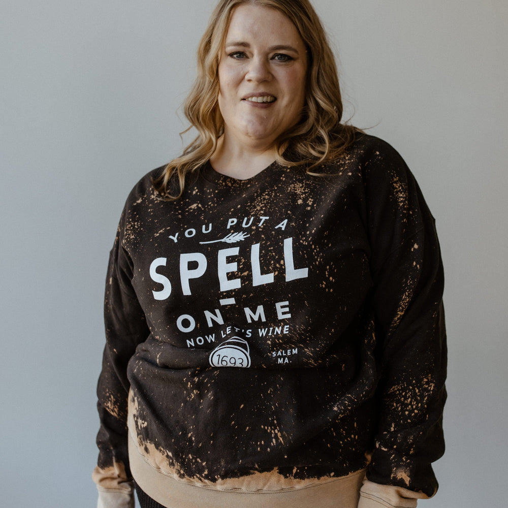 A person with long hair is wearing the Love Marlow "YOU PUT A SPELL ON ME NOW LET'S WINE" graphic sweatshirt, standing against a plain background.