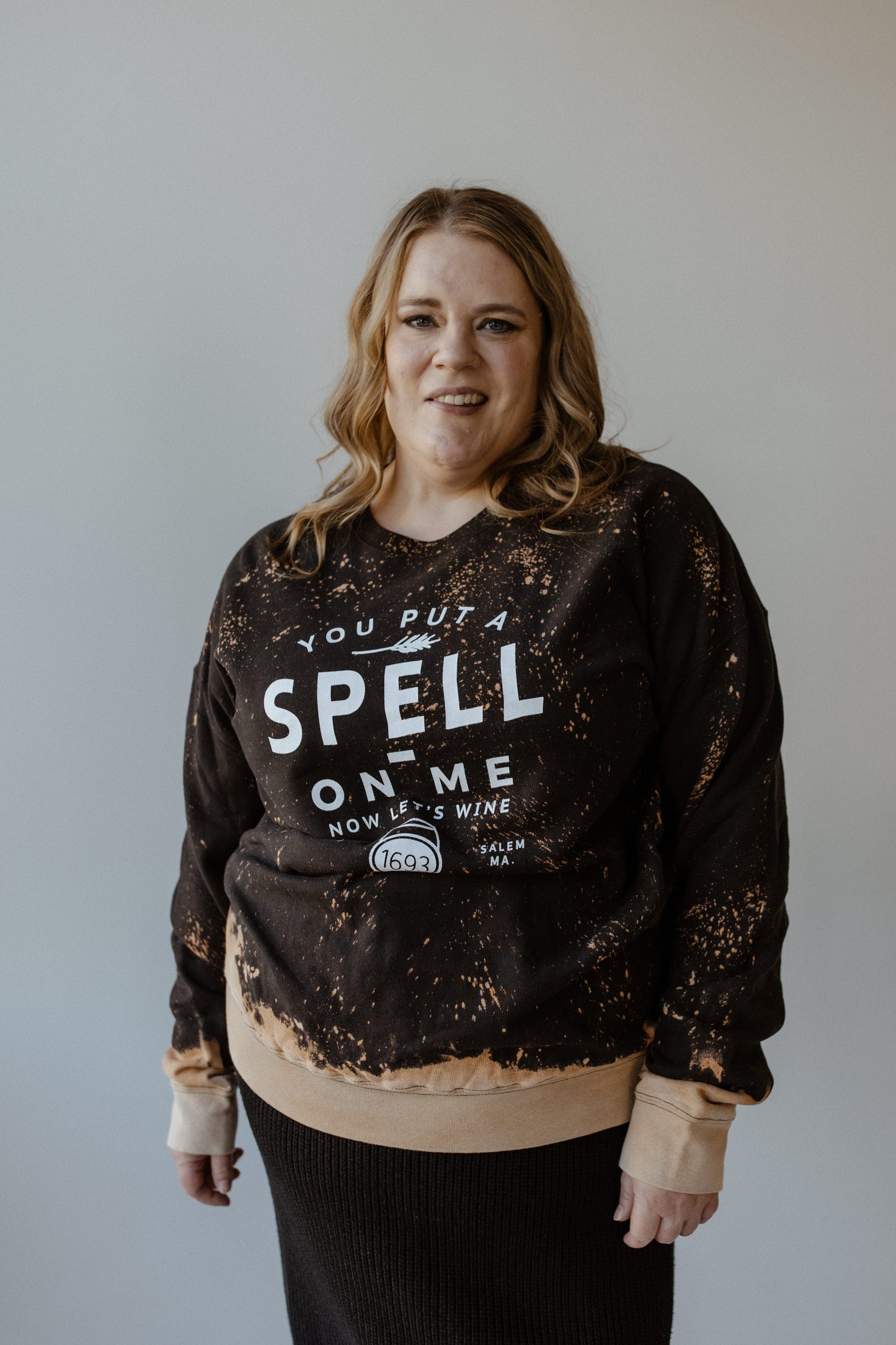 A person with long hair is wearing the Love Marlow "YOU PUT A SPELL ON ME NOW LET'S WINE" graphic sweatshirt, standing against a plain background.