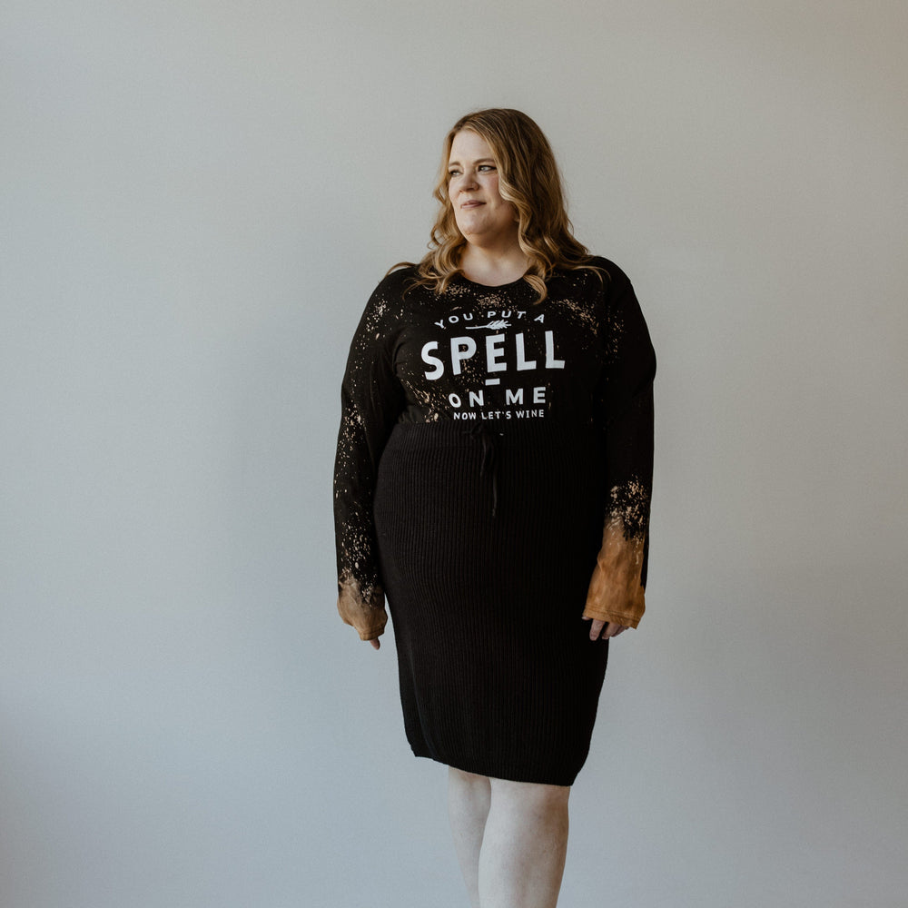 A person dressed in Love Marlow's long sleeve graphic tee, featuring the playful text "You Put a Spell on Me Now Let's Wine," stands against a plain backdrop, exuding Halloween vibes.