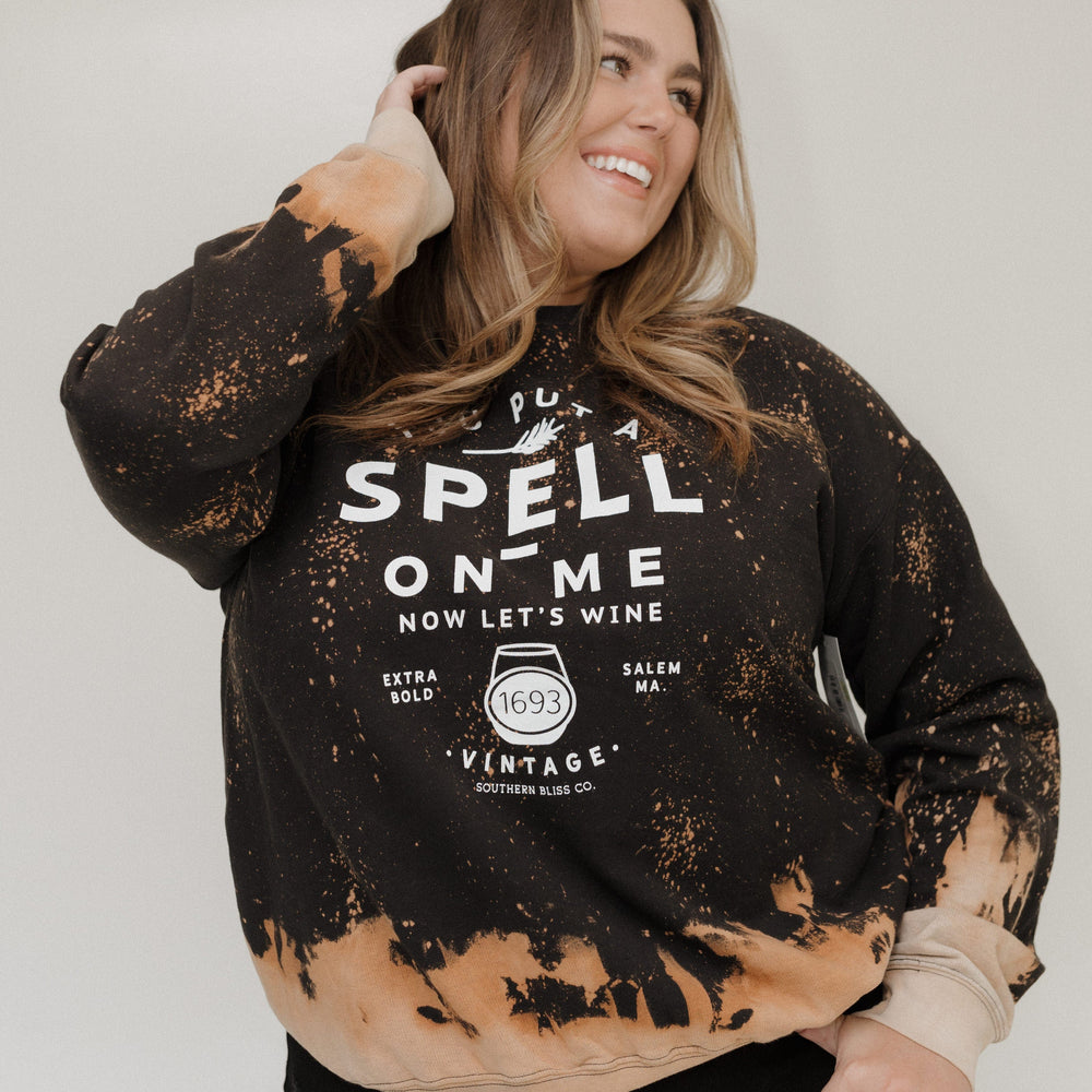 "YOU PUT A SPELL ON ME NOW LET'S WINE" GRAPHIC SWEATSHIRT Woman wearing a black and brown distressed sweatshirt with text on a white background at Love Marlow