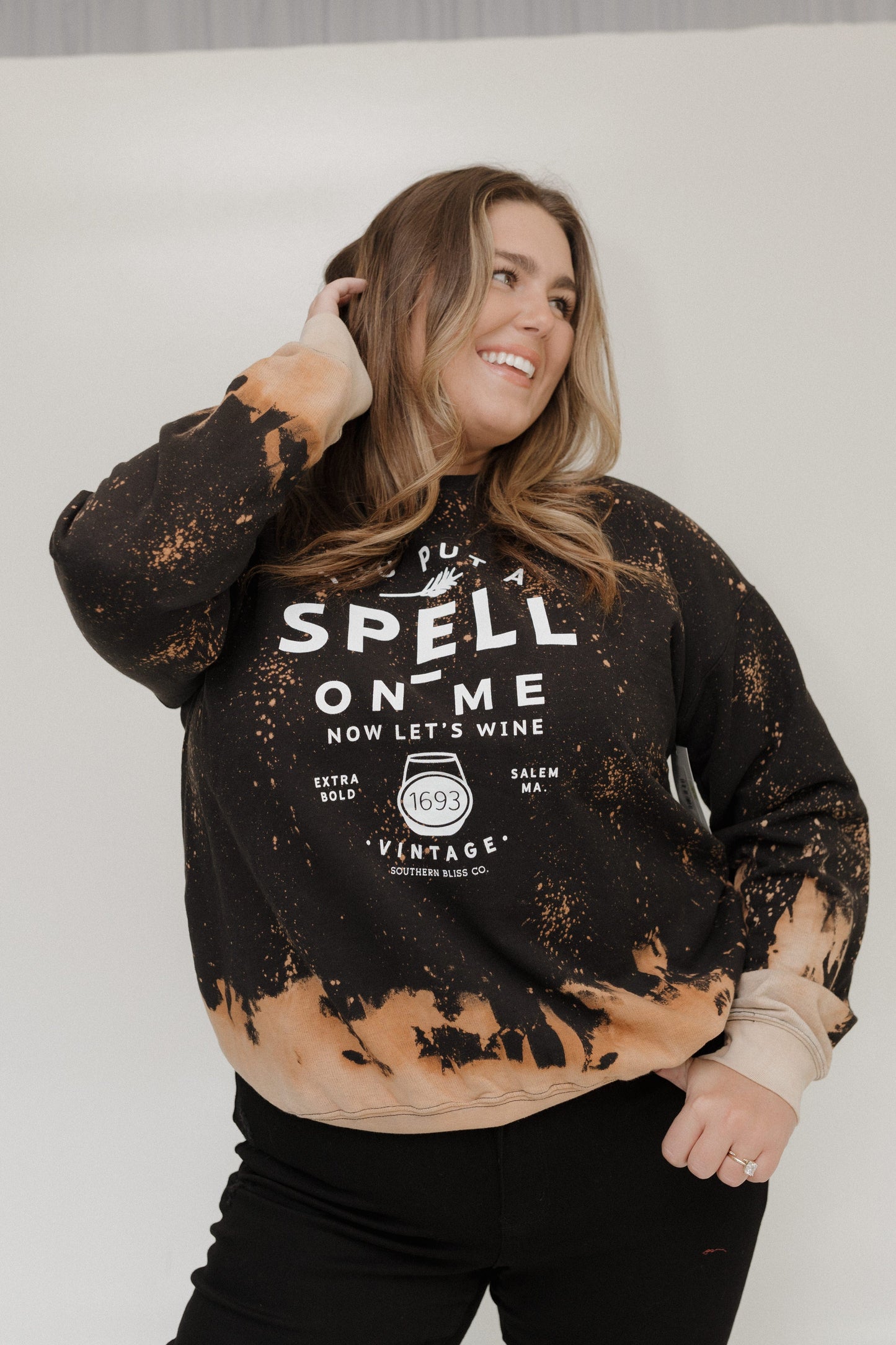 "YOU PUT A SPELL ON ME NOW LET'S WINE" GRAPHIC SWEATSHIRT Woman wearing a black and brown distressed sweatshirt with text on a white background at Love Marlow