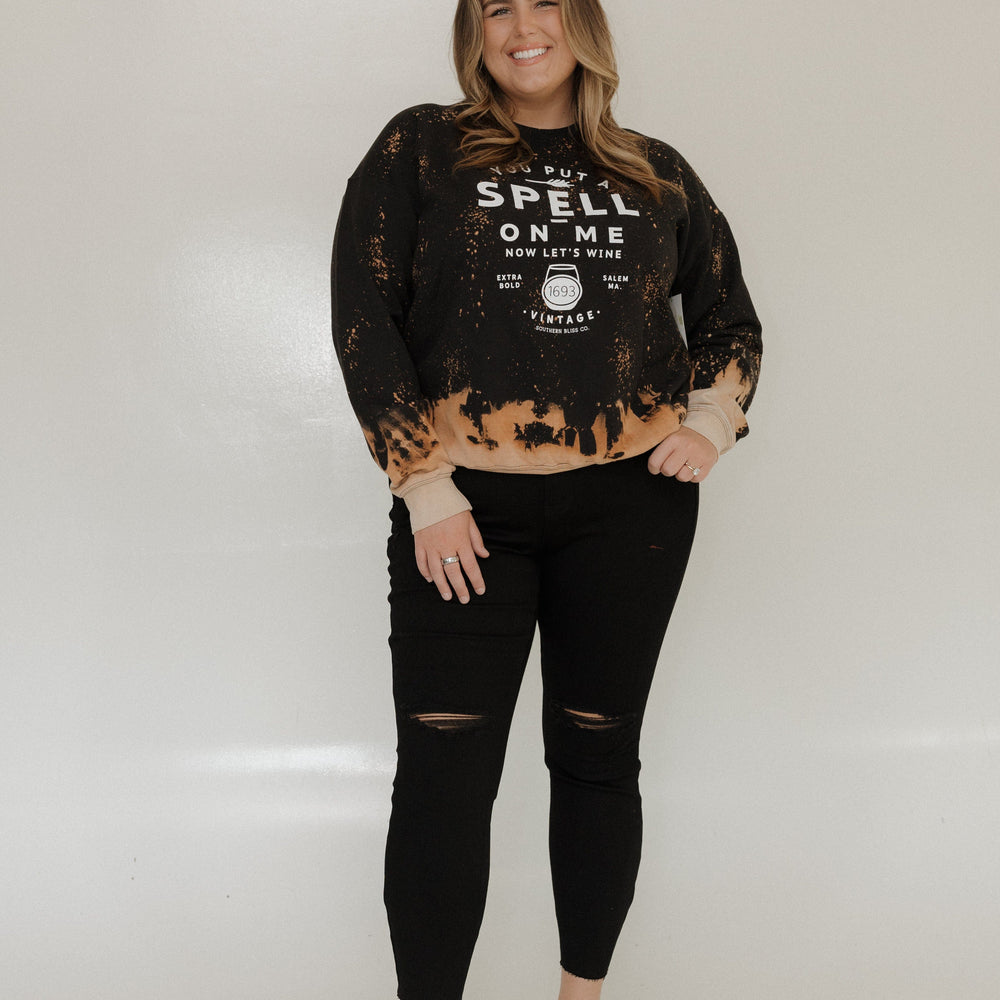 "YOU PUT A SPELL ON ME NOW LET'S WINE" GRAPHIC SWEATSHIRT Woman wearing a black and brown distressed sweatshirt with text on a white background at Love Marlow