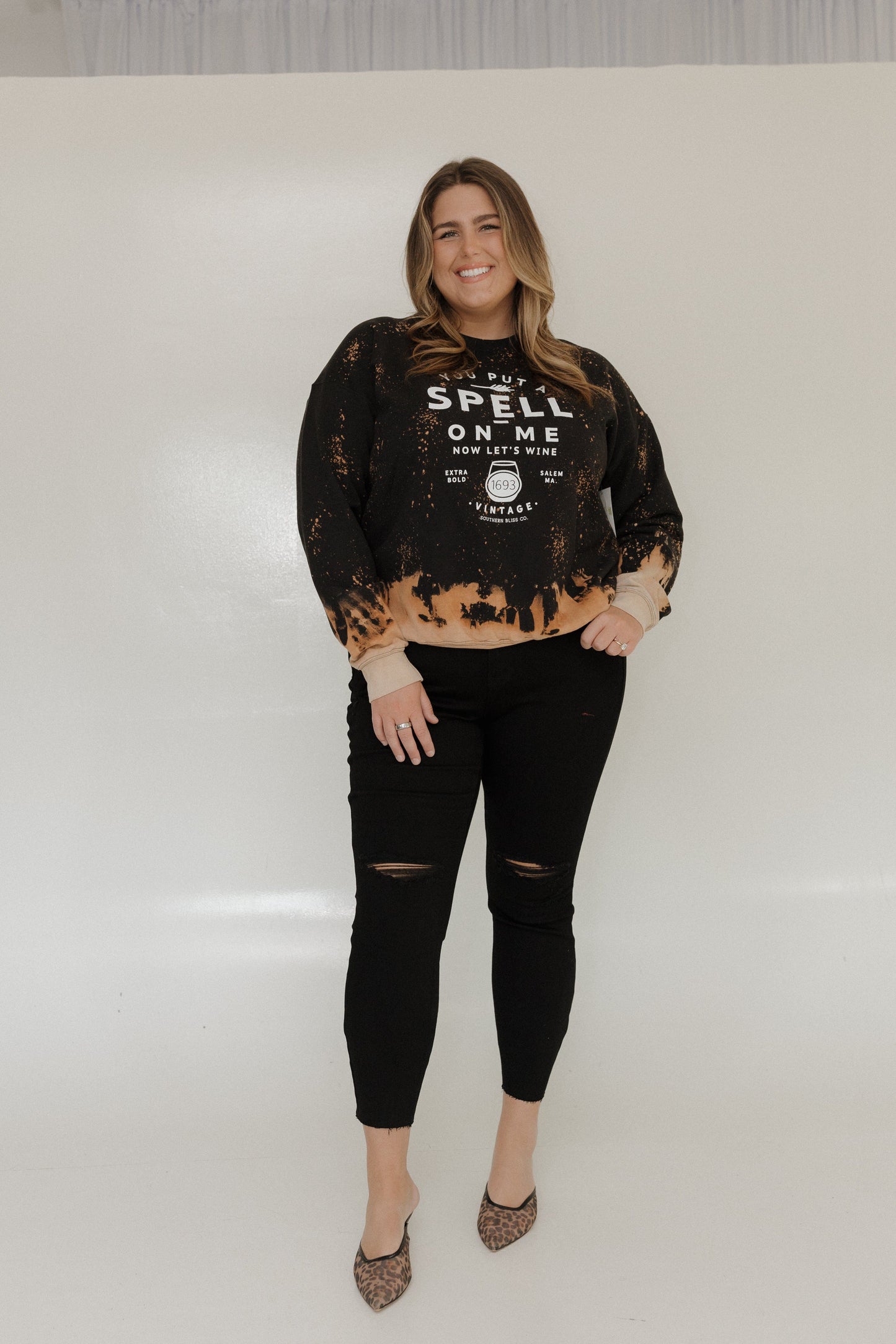 "YOU PUT A SPELL ON ME NOW LET'S WINE" GRAPHIC SWEATSHIRT Woman wearing a black and brown distressed sweatshirt with text on a white background at Love Marlow