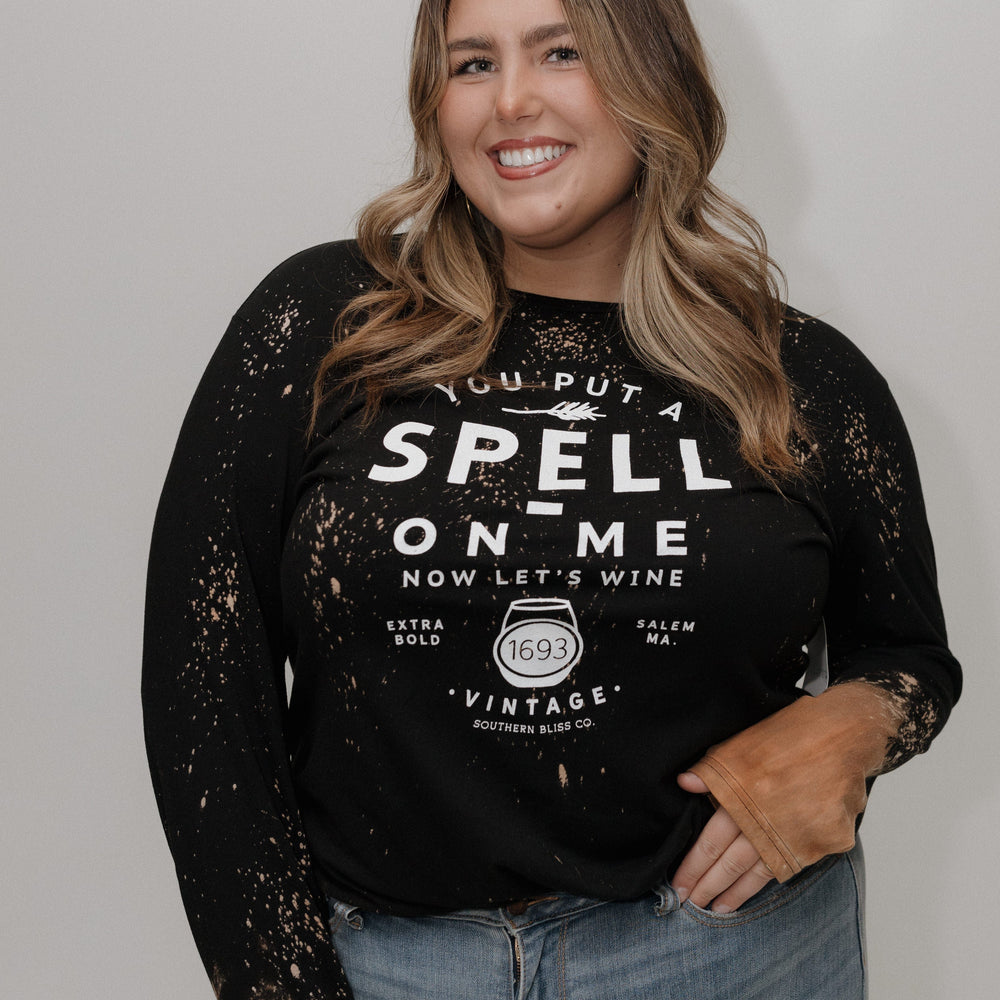 "YOU PUT A SPELL ON ME NOW LET'S WINE" LONG SLEEVE GRAPHIC TEE Woman wearing a black sweatshirt with text and sheer sleeves against a white background at Love Marlow