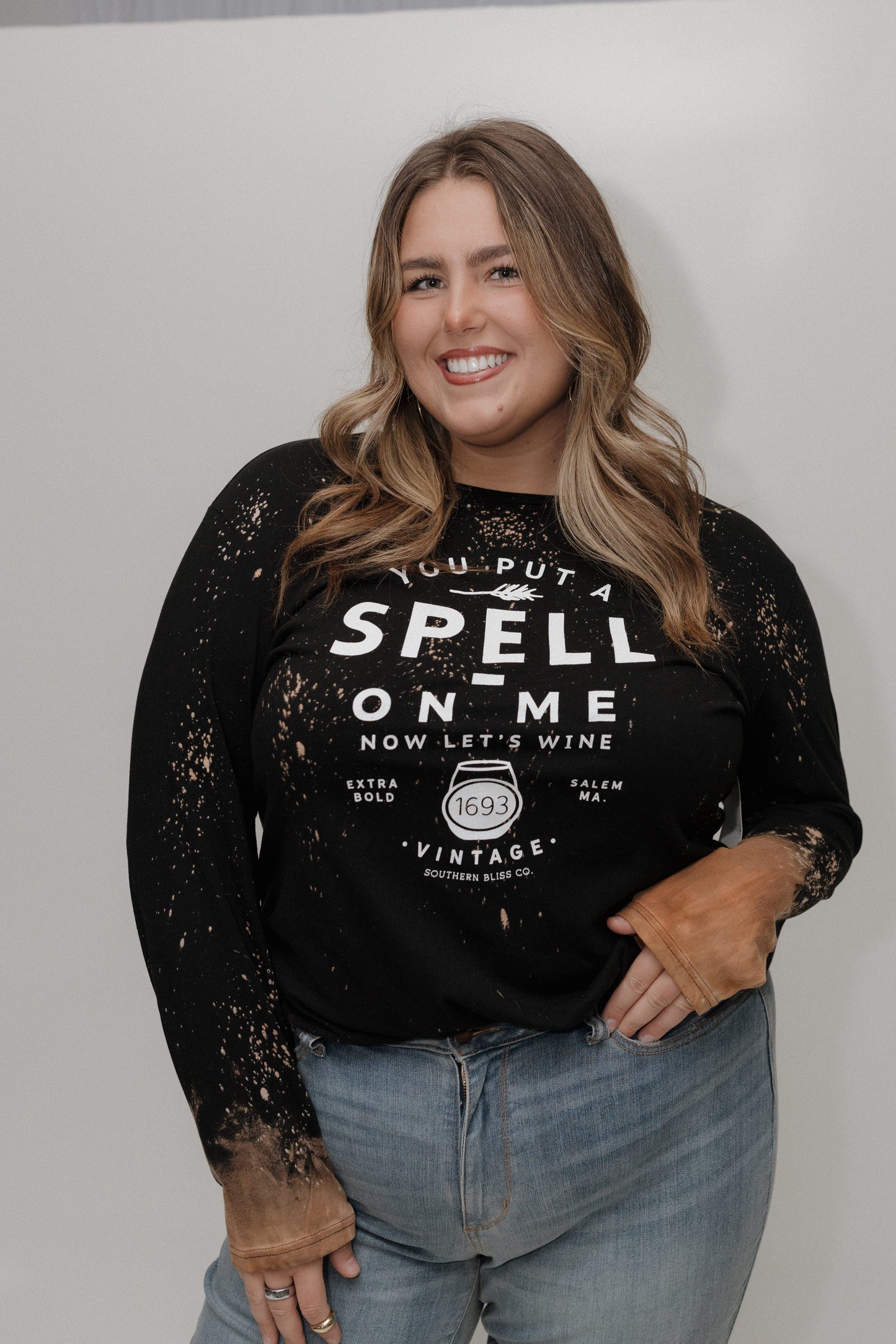 "YOU PUT A SPELL ON ME NOW LET'S WINE" LONG SLEEVE GRAPHIC TEE Woman wearing a black sweatshirt with text and sheer sleeves against a white background at Love Marlow