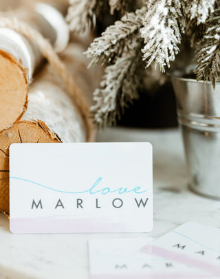 Love Marlow gift card leaning against birch logs with a snowy holiday tree