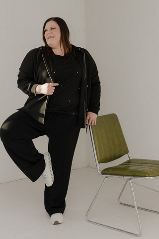 Woman in black outfit posing in a minimal white room with a green chair.