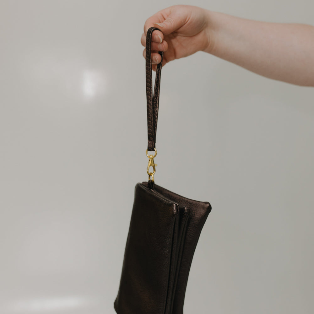 Hand holding a black leather clutch with a gold clasp against a neutral background