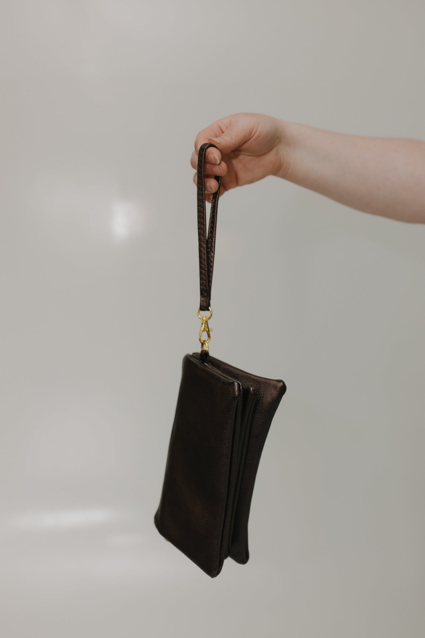 Hand holding a black leather clutch with a gold clasp against a neutral background