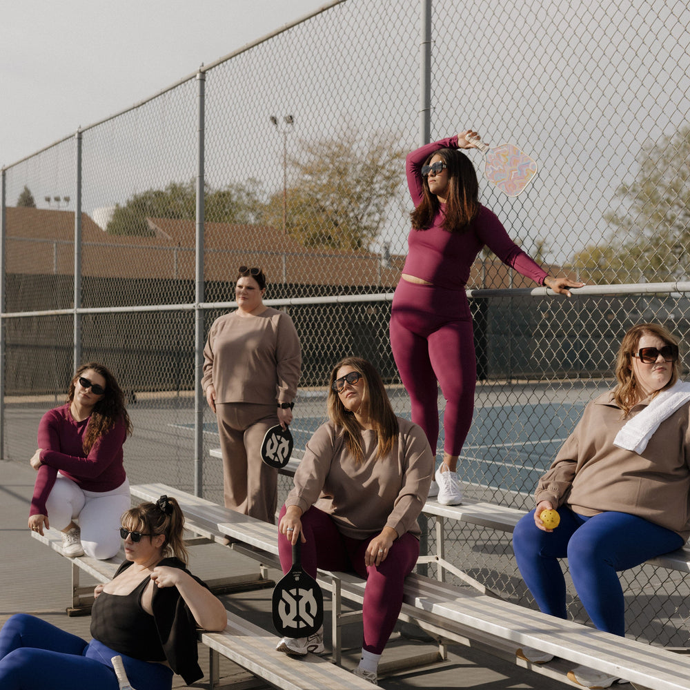 Group of women on bleachers with sports equipment on a tennis court