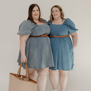 Two women wearing matching blue denim dresses standing side by side against a white background.