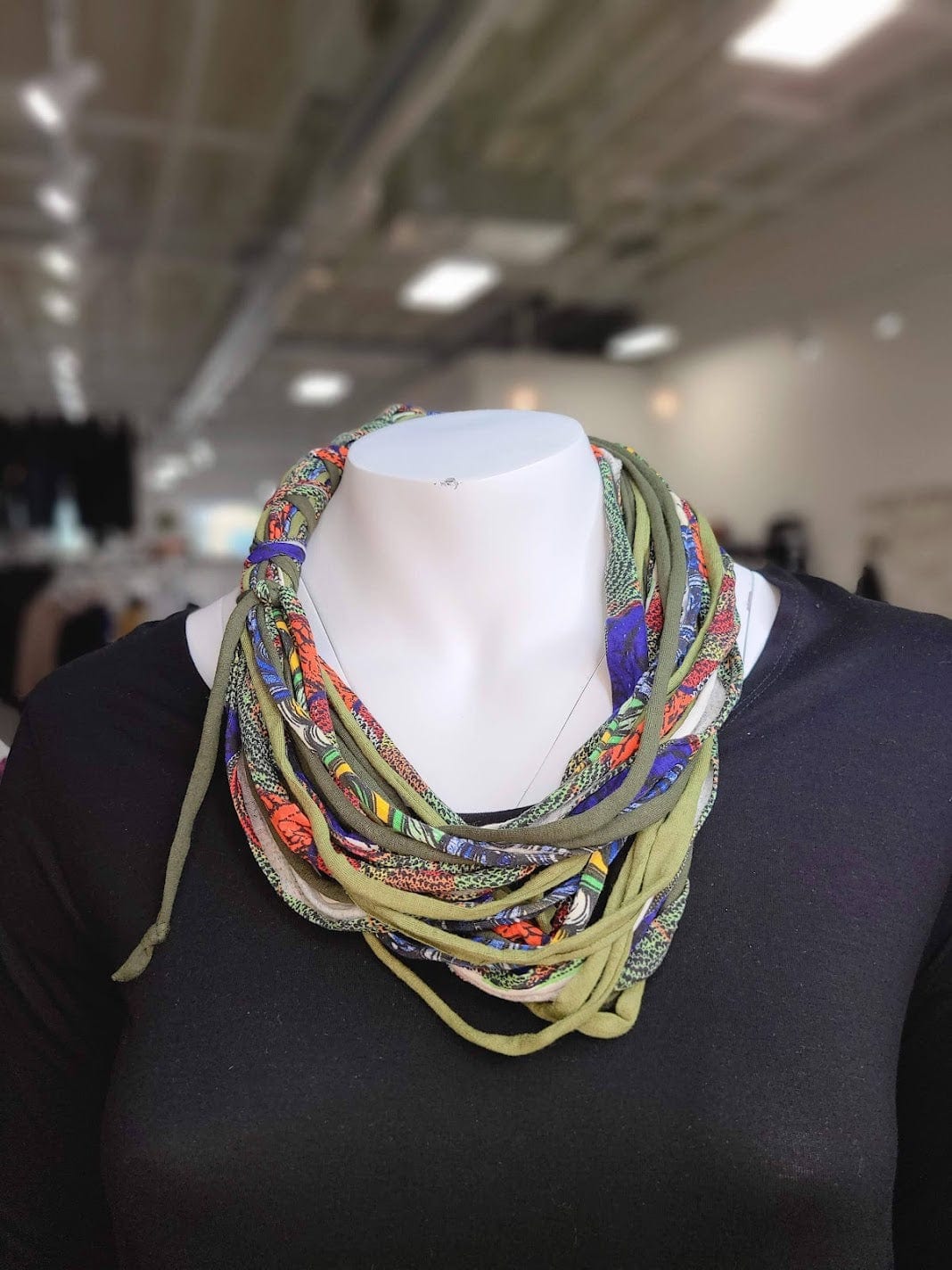 A mannequin showcases a multicolored, layered fabric necklace crafted from textile remnants, elegantly draped over a black top.