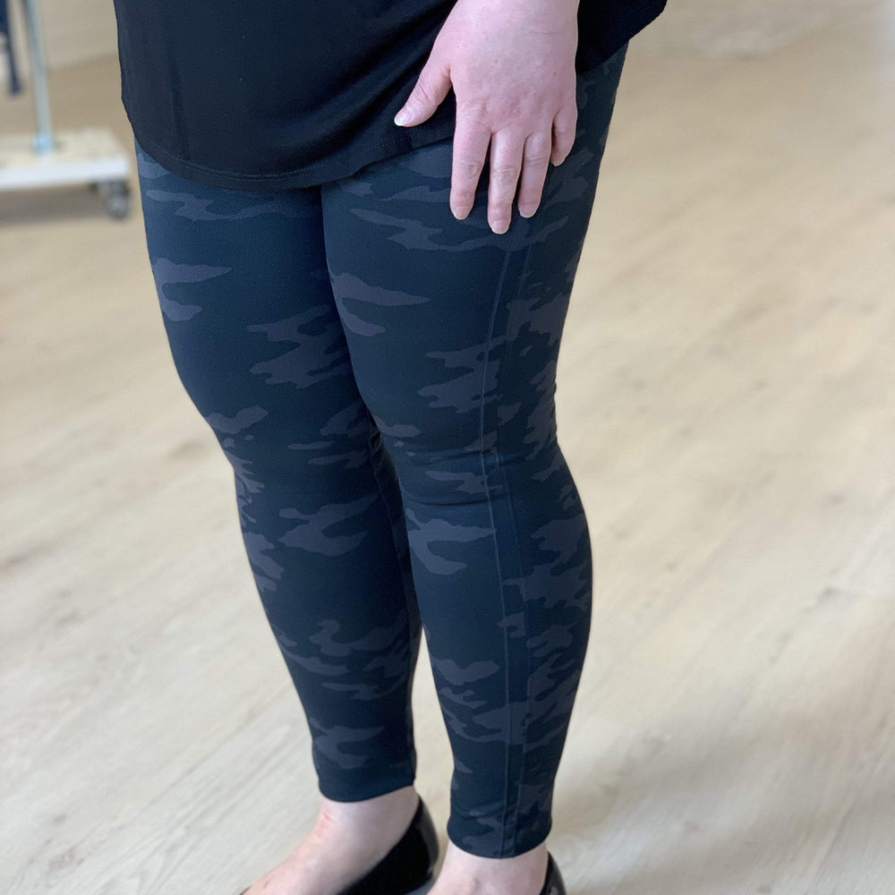 A person wearing a black camisole and Spanx© LOOK AT ME NOW SEAMLESS LEGGING, featuring a double-layer waistband for shaping support, paired with black flats, is standing on a light wooden floor.