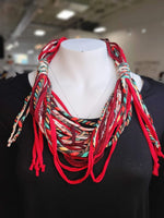 A mannequin displays a statement necklace crafted from twisted, multicolored cords over a plain black top, elegantly paired with a scarf made from leftover fabric.