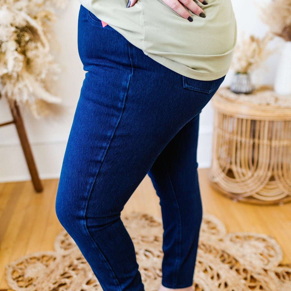 Person wearing Love Marlow Spanx© ANKLE JEAN-ISH® LEGGING and a light green top, standing barefoot on a woven rug in a room with wooden flooring and decorative dried plants.