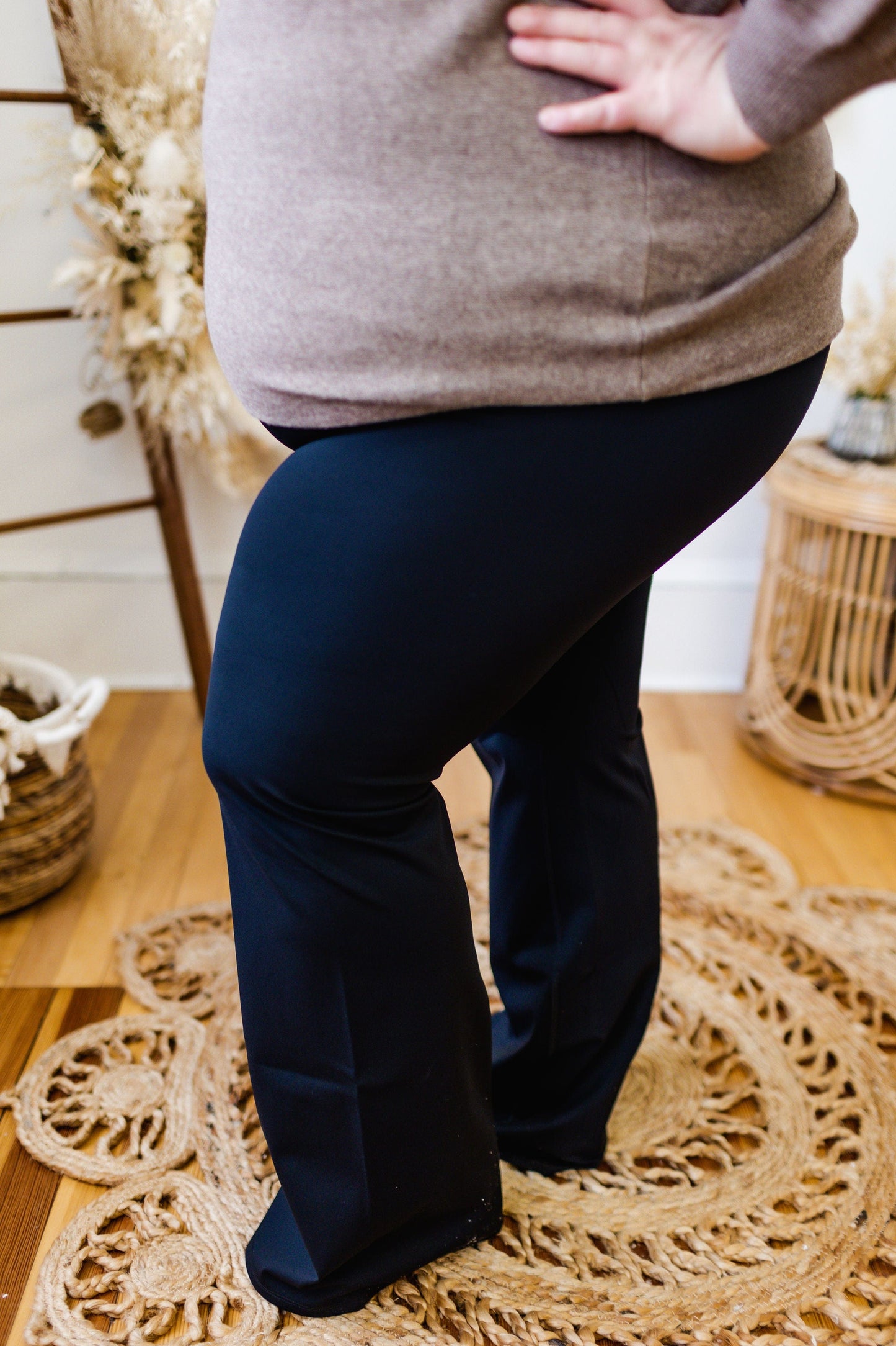 A person wearing the Love Marlow Spanx© BOOTY BOOST YOGA PANT, featuring a contoured waistband, stands indoors on a woven rug, one hand confidently on their hip.