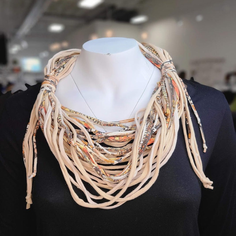 A mannequin displays a statement necklace crafted from twisted, multicolored cords over a plain black top, elegantly paired with a scarf made from leftover fabric.