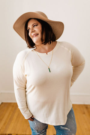 Person wearing a white sweater, jeans, and a beach hat, smiling to the side against a plain background.