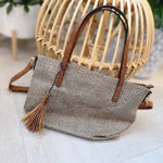 Open beige and brown woven hobo bag with a chevron pattern interior and a small zippered pocket, placed beside a wicker chair on a light wooden floor.