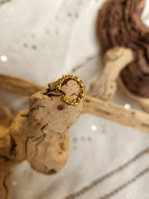 18K Gold Plated twisted ring displayed on rough wooden branches against a textured white fabric background, showcasing its hypoallergenic design.