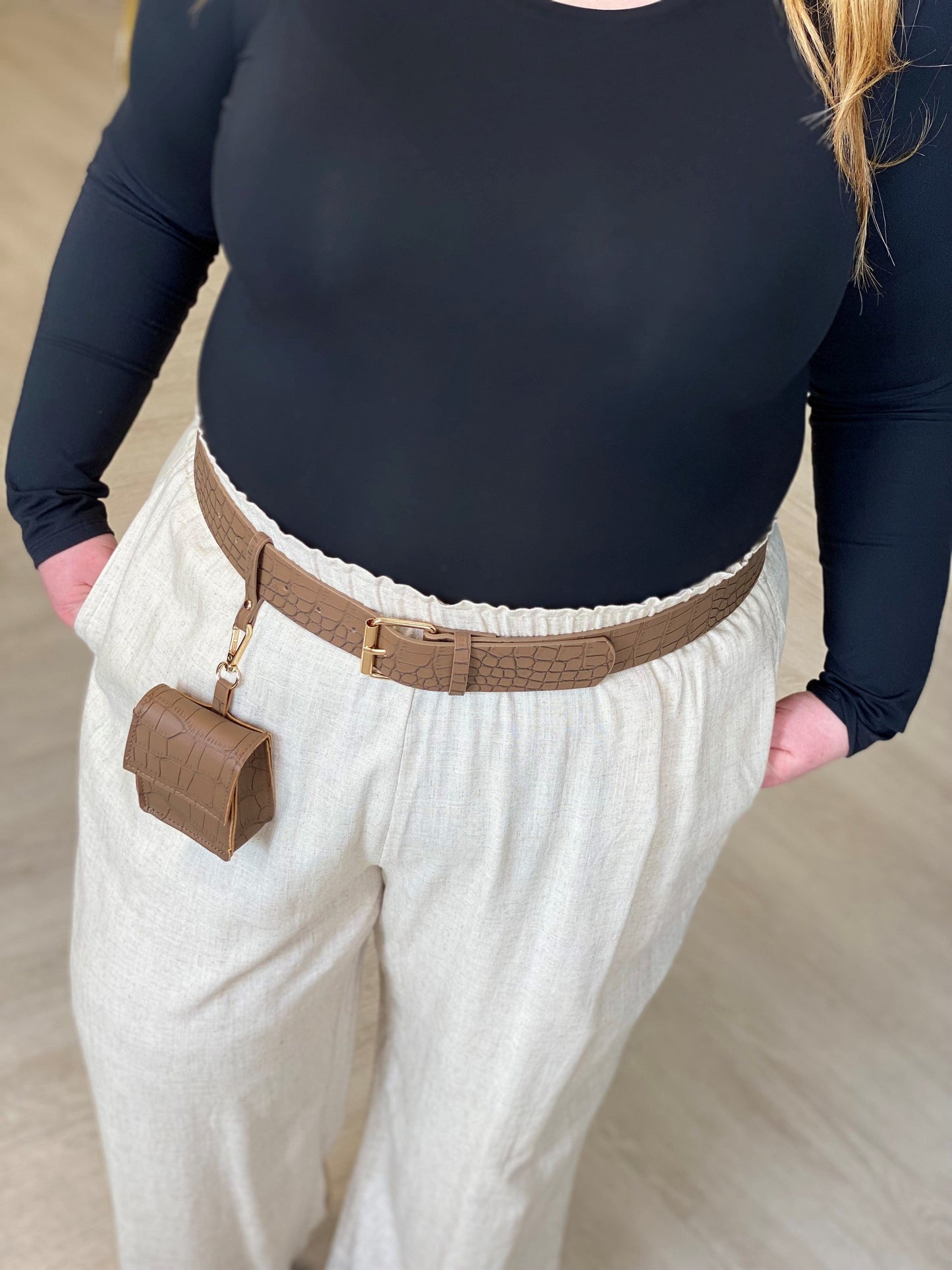 A person wearing a black long-sleeve top and light beige pants, complemented by a crocodile-embossed leather belt and featuring a small attached pouch.