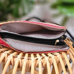 An open pink clutch with a black faux leather wallet inside rests gracefully on a wicker chair.