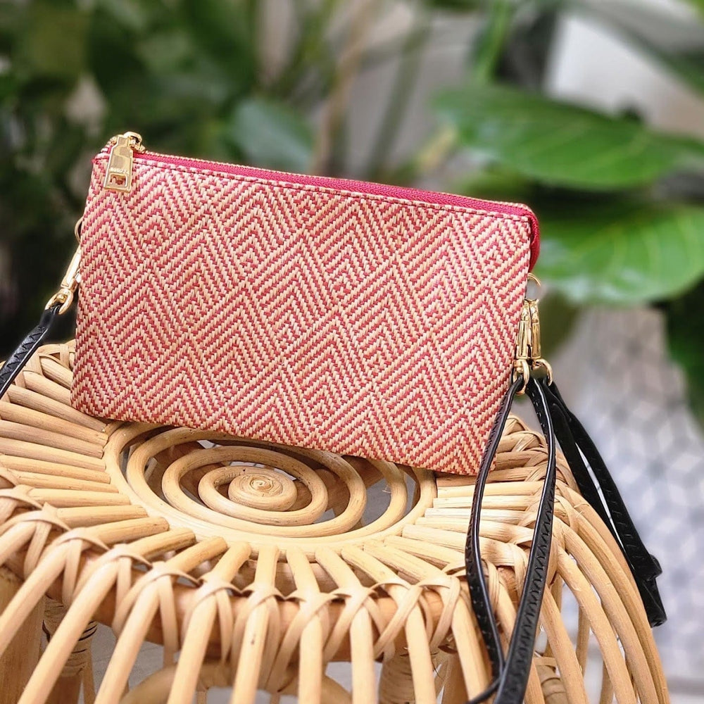 A pink and white woven clutch with gold hardware and a detachable faux leather strap elegantly rests on a wicker chair.